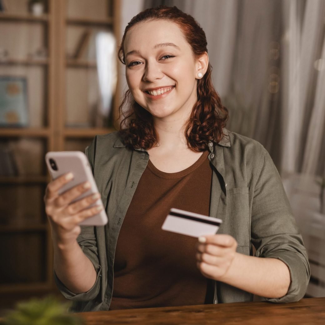 smiley-woman-using-credit-card-smartphone-home
